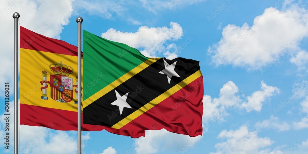 Spain and Saint Kitts And Nevis flag waving in the wind against white cloudy blue sky together. Diplomacy concept, international relations. Spain and Saint Kitts And Nevis flag waving in the wind against white cloudy blue sky together. Diplomacy concept, international relations.