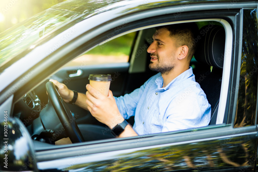 Naklejka premium Young man drinking coffee while driving the car