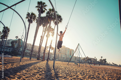 A young man athlete working out on traveling rings on muscle beach, Santa Monica, California photo