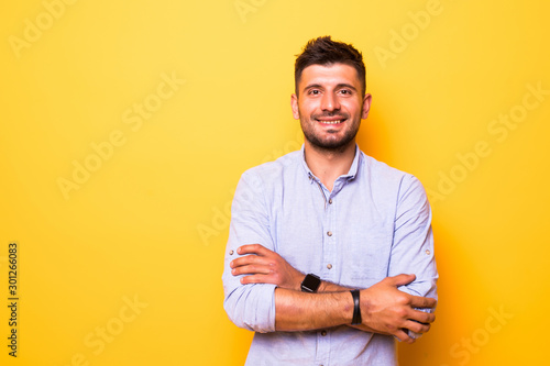 Portrait of a smiling bearded man standing with arms folded over yellow background