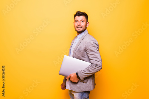 Young man with a laptop isolated on a yellow background