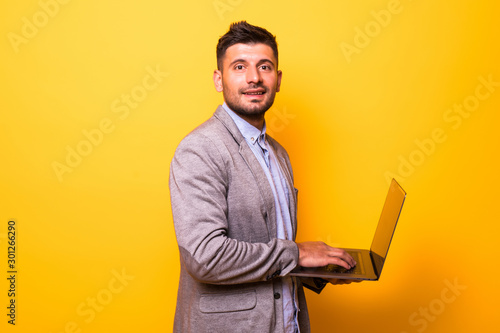 Young handsome man with laptop on yellow background