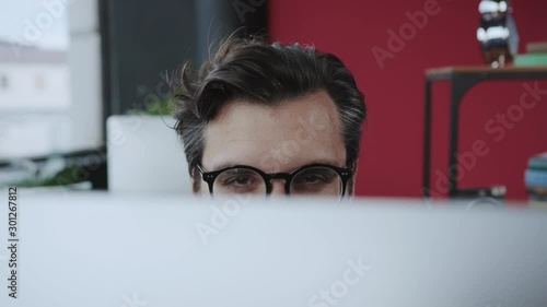 Close-up funny tricky office manager showing eyes behind monitor flirting or spying working at desktop computer. Fun time. Office people.