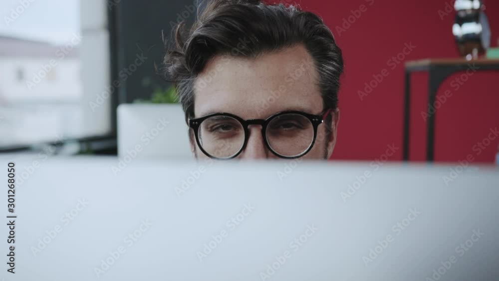 Fun scene in the office. Close-up tricky manager director appearing behind monitor winking with eye flirting on camera while working. Fun scene in the office. Close-up tricky manager director appearing behind monitor winking with eye flirting on camera while working.