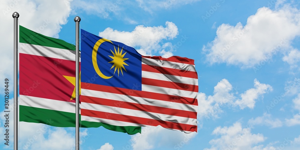 Suriname and Malaysia flag waving in the wind against white cloudy blue sky together. Diplomacy concept, international relations.