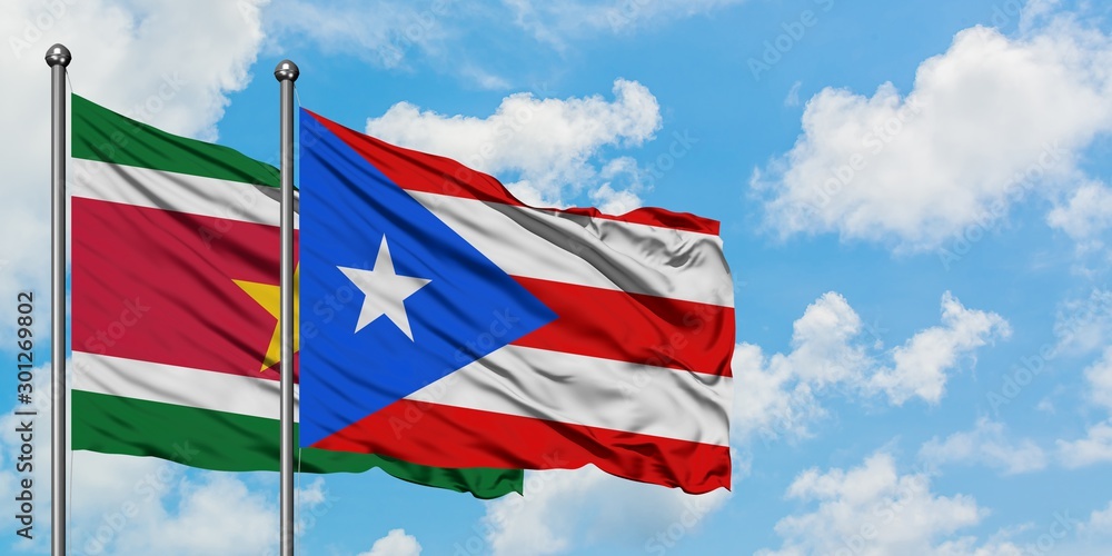 Suriname and Puerto Rico flag waving in the wind against white cloudy blue sky together. Diplomacy concept, international relations.