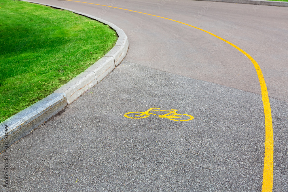 Obraz premium Bicycle symbol on an asphalt road with a dedicated lane for bicycle traffic, an empty road with a curb and green grass on the side of the road.