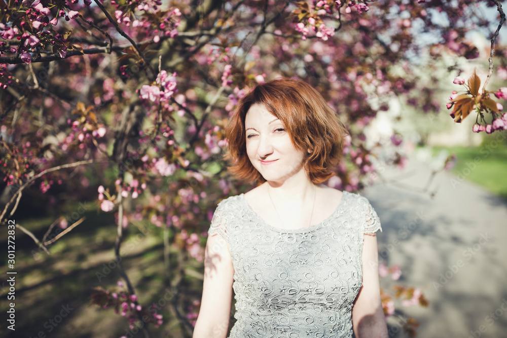 Cheerful middle aged Armenian woman in an elegant dress under the blooming sakura tree. Cheerful middle aged Armenian woman in an elegant dress under the blooming sakura tree.
