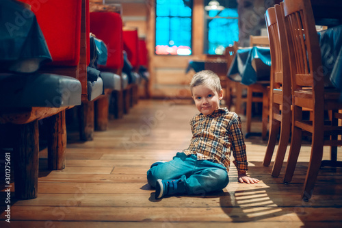 Cute adorable boy three years old having fun in cafe restaurant. Child sitting on floor in public place. Freedom of self expression and behaviour for kids. Toddler touching dirty ground.