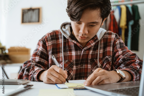 asian young business store owner taking note from customer. online business store working from home