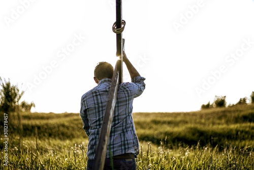 Male carrying a hand made wooden cross in a grassy field shot from behind photo