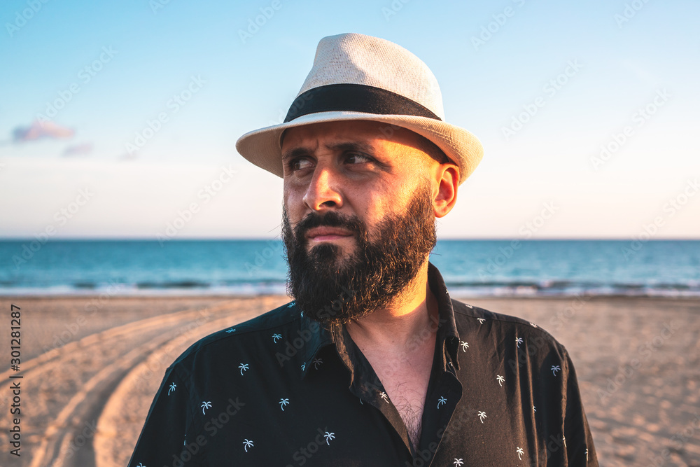 Portrait of a man with a beard and a white hat on a beach