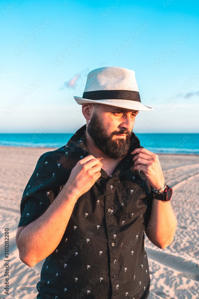 Portrait of a man with a beard and a white hat, putting on his shirt