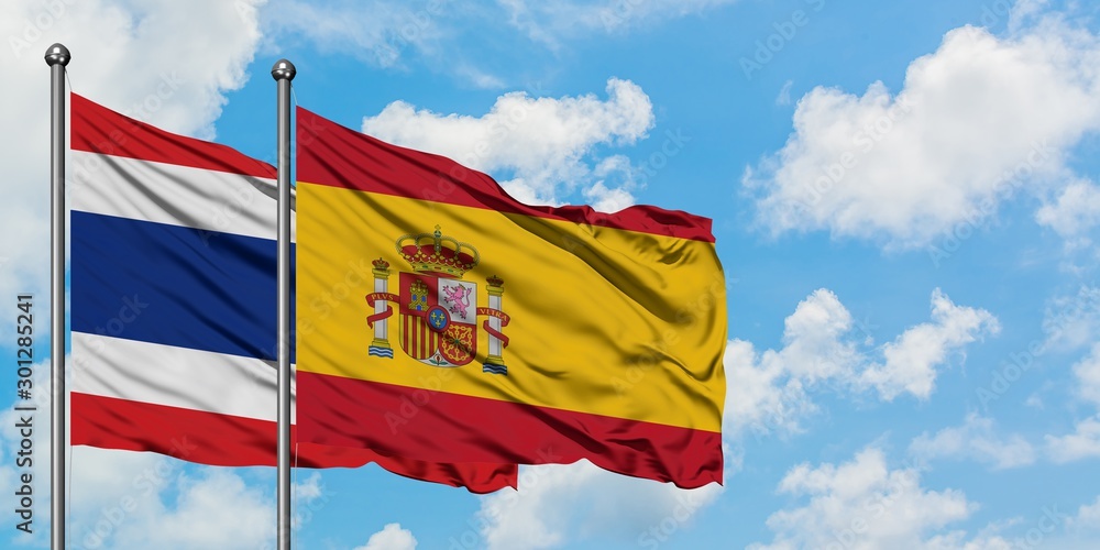 Thailand and Spain flag waving in the wind against white cloudy blue sky together. Diplomacy concept, international relations. Thailand and Spain flag waving in the wind against white cloudy blue sky together. Diplomacy concept, international relations.