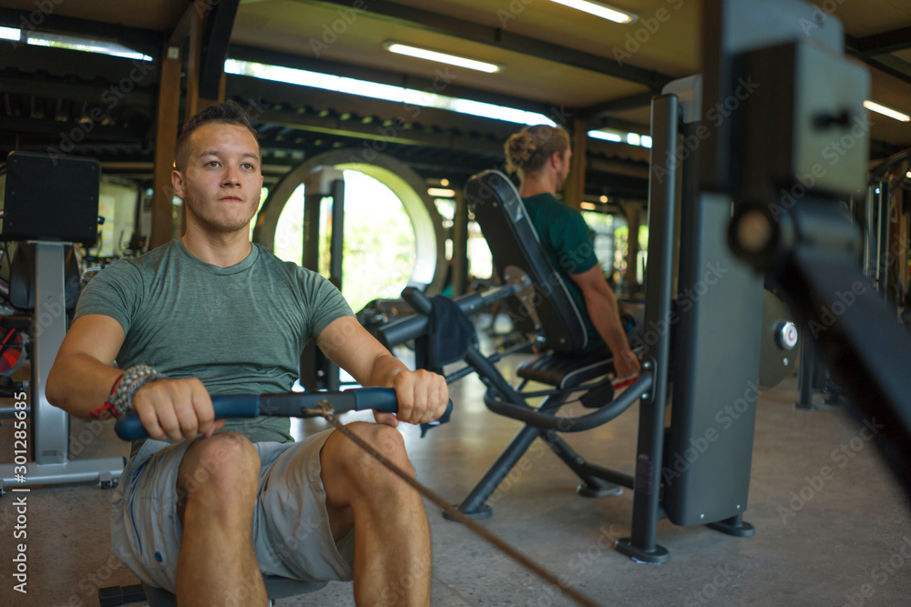  young athletic and attractive man training body building doing rowing exercise in row machine pulling hard with determination and energy  at gym club