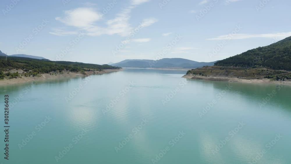 Aerial Drone shot of beautiful blue turquoise Lake Yesa with water reflections near spanish mountains in Spain, blue sky, clouds and trees landscape, valley, volcanic, green nature, 4K. Tracking in. Aerial Drone shot of beautiful blue turquoise Lake Yesa with water reflections near spanish mountains in Spain, blue sky, clouds and trees landscape, valley, volcanic, green nature, 4K. Tracking in.