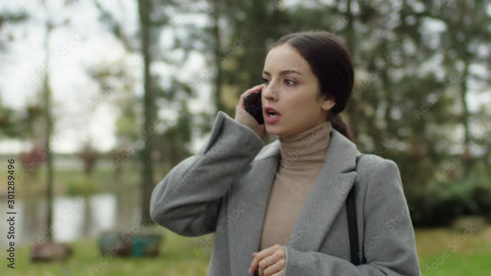 Displeased young woman in grey coat expressing outrage while talking on mobile phone over nice autumn parkland. Girl argues and tries to prove her case Displeased young woman in grey coat expressing outrage while talking on mobile phone over nice autumn parkland. Girl argues and tries to prove her case