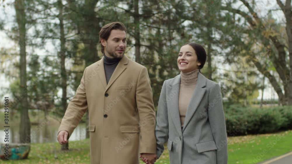 A beautiful couple of lovers walk along a park alley. Young people in business clothes hold hands, talk and enjoy the beautiful weather. A beautiful couple of lovers walk along a park alley. Young people in business clothes hold hands, talk and enjoy the beautiful weather.