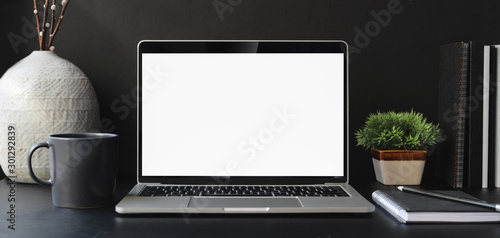 Open blank screen laptop computer in dark modern office room with office supplies