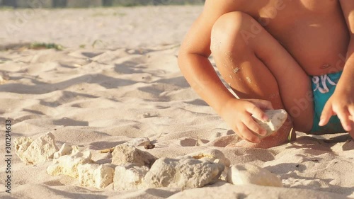 Cute boy playing with rocks on sandy beach.