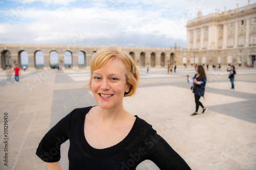 A woman enjoys traveling in Spain and poses for photos in the beautiful Plaza de la Armería in front of the Royal Palace.