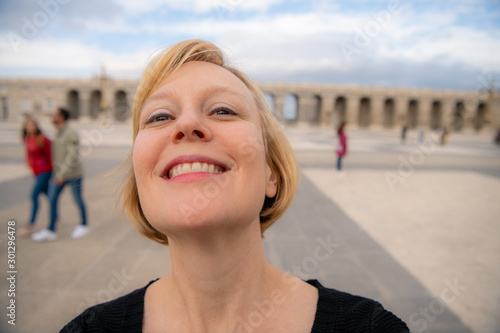 A woman enjoys traveling in Spain and poses for photos in the beautiful Plaza de la Armería in front of the Royal Palace. She spins with the camera.