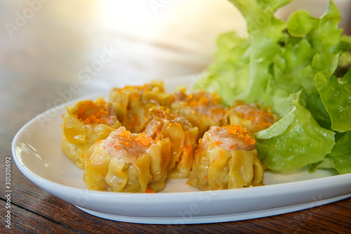 Selective focus of Chinese Steamed Dumpling topped with Flying fish roe on white dish served with lettuce leaves.