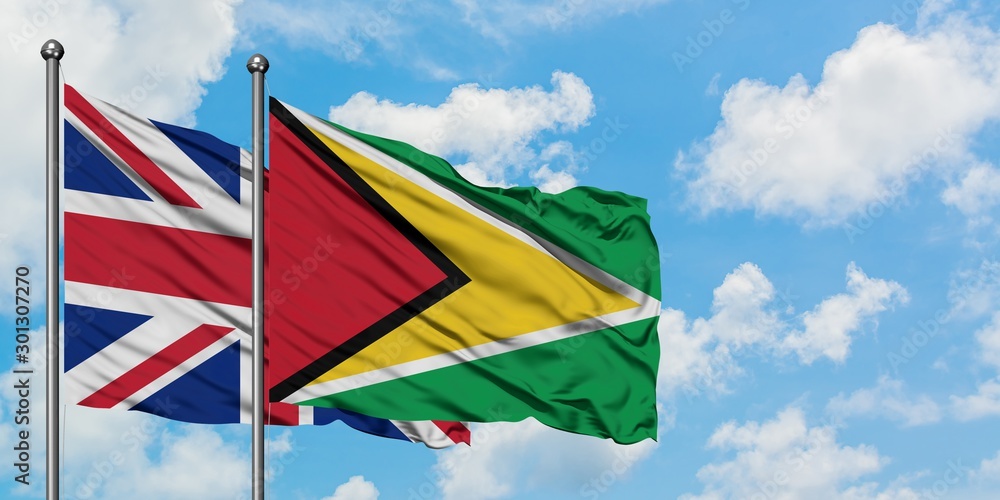 United Kingdom and Guyana flag waving in the wind against white cloudy blue sky together. Diplomacy concept, international relations.