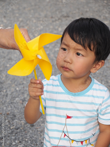 Asian lovely kid holding and playing a yellow windmill toy with dad with small stones background. Cute young boy learning how turbine blow. Freedom and happy time. Preschool learning concept.