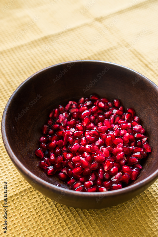 Pomegranate Seeds in Wooden Bowl with Natural Sunlight and Pastel Yellow Tablecloth. Natural Sunlight. Pomegranate Seeds in Wooden Bowl with Natural Sunlight and Pastel Yellow Tablecloth. Natural Sunlight.