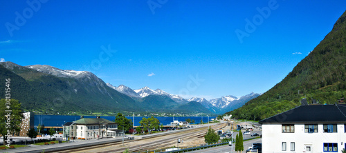 Railroad tracks along the fjord at Andalsnes, Norway with mountains with snow and blue sky in the background on a sunny day.