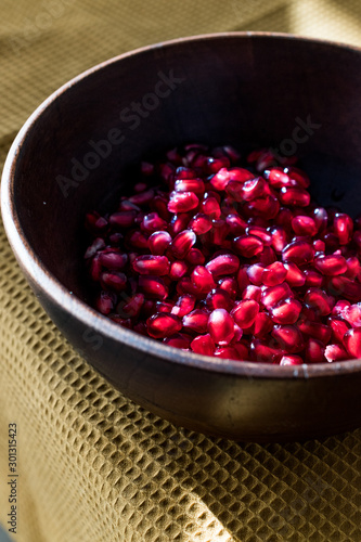 Pomegranate Seeds in Wooden Bowl with Natural Sunlight and Pastel Yellow Tablecloth. Natural Sunlight.