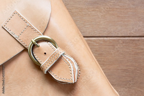 detail of genuine leather bag with fastened buckle strap on wooden table, close up. fashion concept. photo