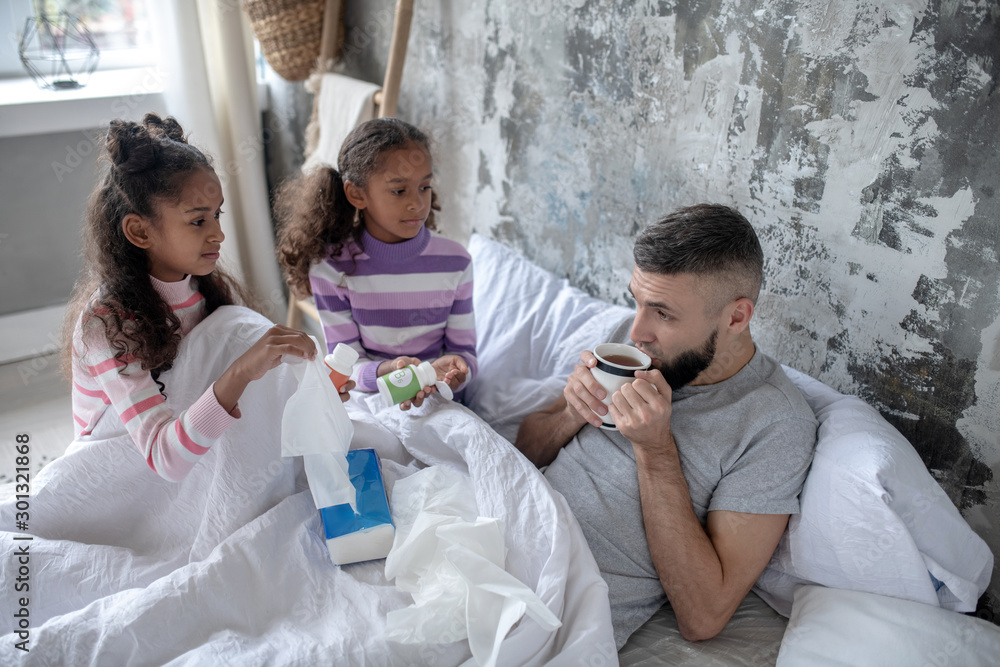 Daughters bringing hot tea and vitamins for their sick daddy Daughters bringing hot tea and vitamins for their sick daddy