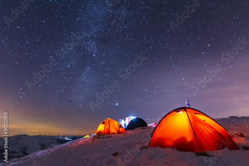 Great bright campsite with colorful tourist tents, on top in the Ukrainian Carpathian Mountains, at night with views of the stars and the Milky Way