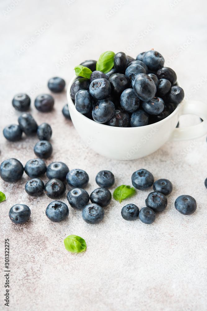 Blueberries lie in a Cup and scattered on a concrete table. Summer seasonal product. Healthy vegetarian dessert. Blueberries lie in a Cup and scattered on a concrete table. Summer seasonal product. Healthy vegetarian dessert.