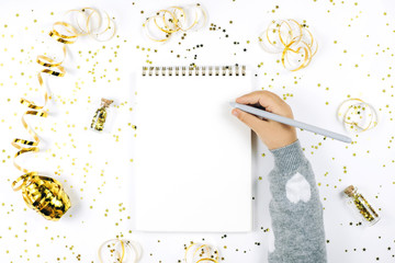 Child's hand writing in notebook on white rustic sparkling background, flat lay style. Christmas planning concept.