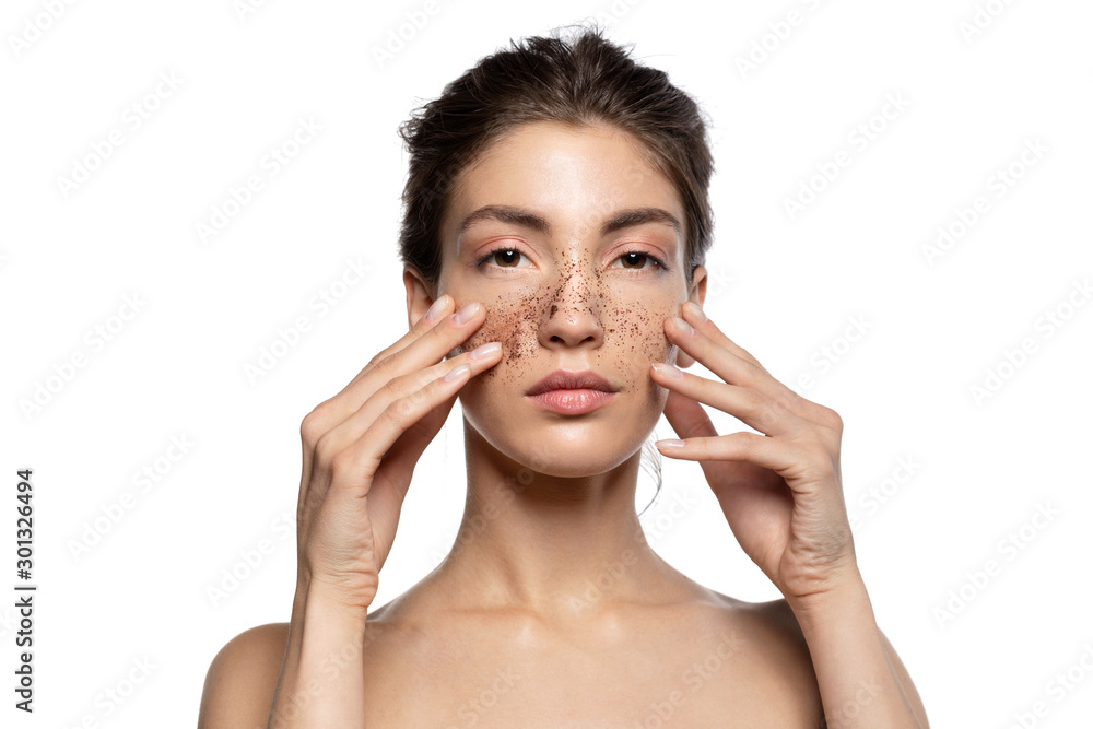 Close up portrait of young woman cleaning face skin with natural scrub. Pretty brunette girl applying cosmetic mask look at camera. Peeling spa procedure, cosmetology. White studio blank copy space Close up portrait of young woman cleaning face skin with natural scrub. Pretty brunette girl applying cosmetic mask look at camera. Peeling spa procedure, cosmetology. White studio blank copy space
