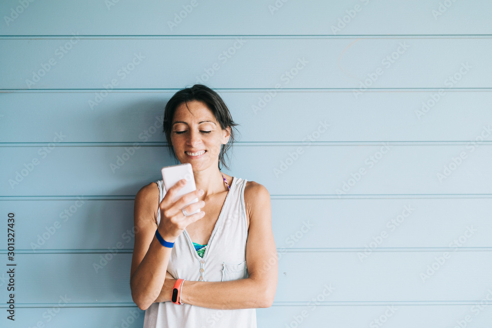 Beautiful adult woman leaning on a wood wall while using a smartphone Beautiful adult woman leaning on a wood wall while using a smartphone