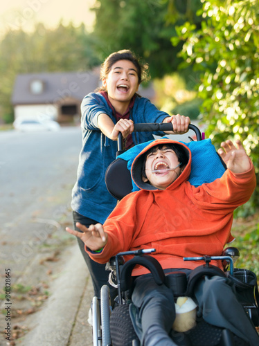 Teen girl pushing disabled boy in wheelchair outdoors, laughing together