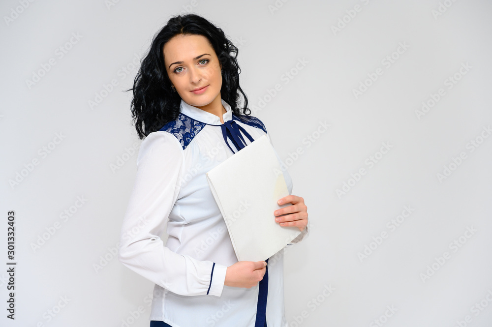 Portrait of a pretty brunette woman with long curly hair on a white background in a white blouse with a folder in her hands. He stands in front of the camera, smiles, talks in various poses. Portrait of a pretty brunette woman with long curly hair on a white background in a white blouse with a folder in her hands. He stands in front of the camera, smiles, talks in various poses.