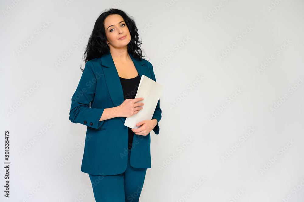 Portrait of a pretty brunette woman with long curly hair on a white background in a business suit with a folder in her hands. He stands in front of the camera, smiles, talks in various poses.
