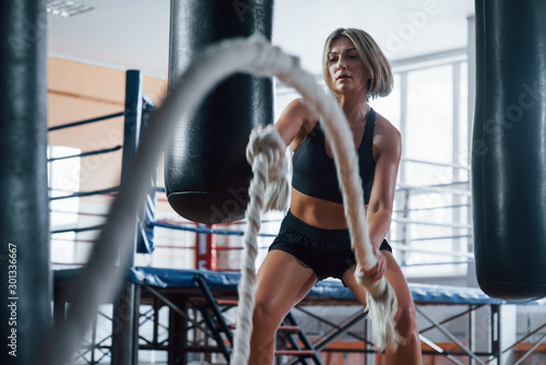 Session with battle ropes. Blonde sport woman have exercise in the gym. Strong female