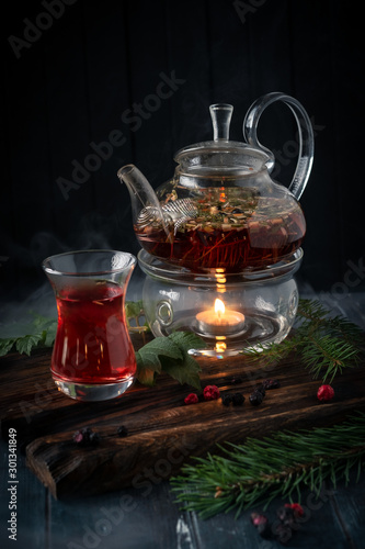 A glass of herbal tea with blackcurrants in a teapot on a dark wooden background. Fragrant natural drink from wild berries.