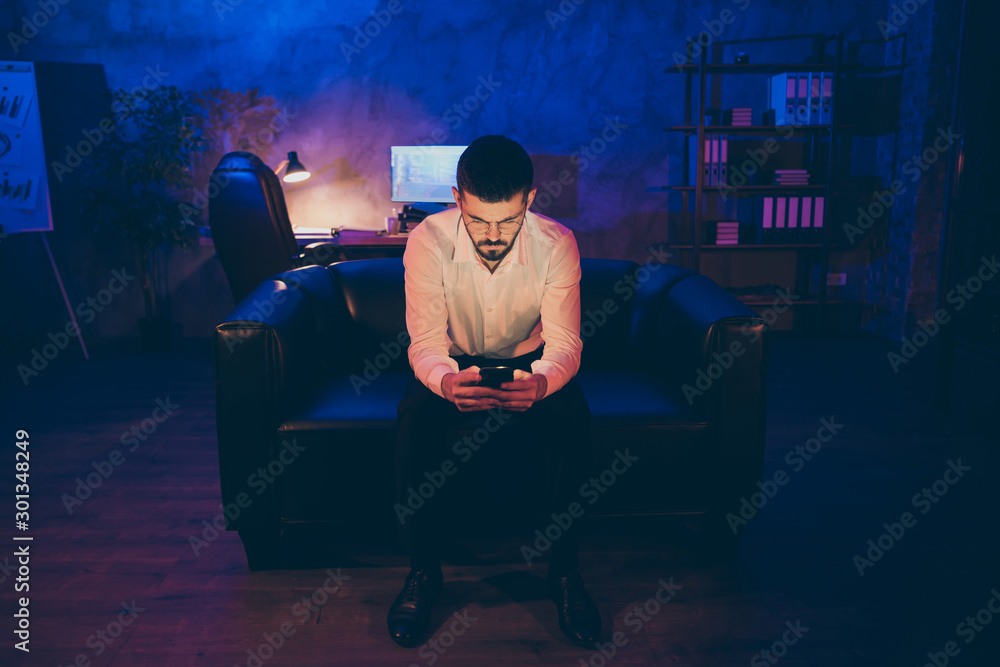 Photo of serious pensive man browsing through his phone to inform colleagues about having finished work having rest after difficult work night Photo of serious pensive man browsing through his phone to inform colleagues about having finished work having rest after difficult work night