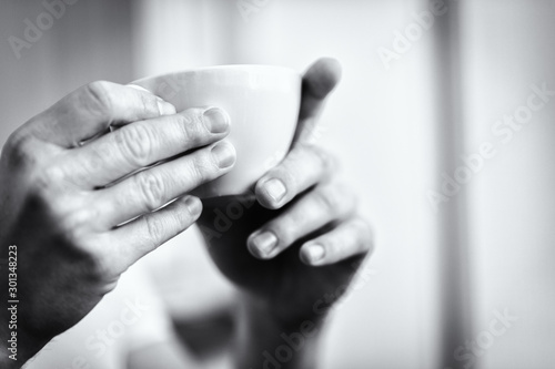 time for a coffee or tea - focus on hands and a white cup in black and white 