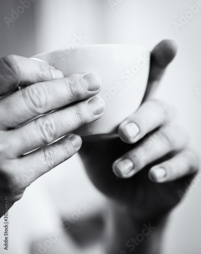 time for a coffee or tea - focus on hands and a white cup in black and white 