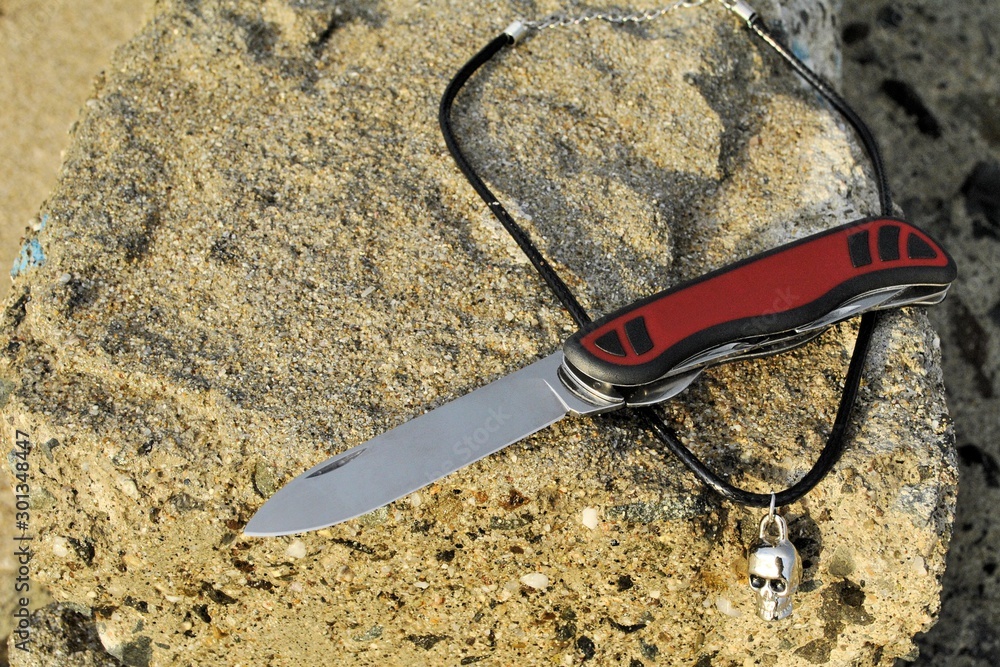 Obraz premium Folding knife stainless blade black red handle travel vacation beach background