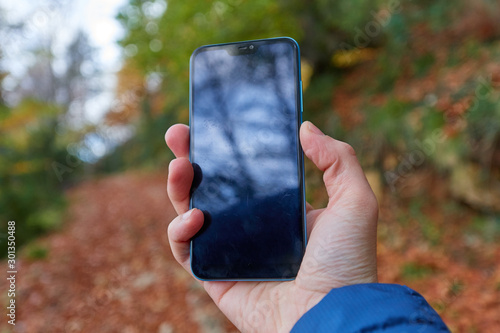 Mobile in someone's right hand, unfocused background with autumnal colors, a path full of brown leaves is intuited photo