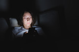 Woman in bed uses phone late at night. Insomnia and text messaging at late hours instead of sleep